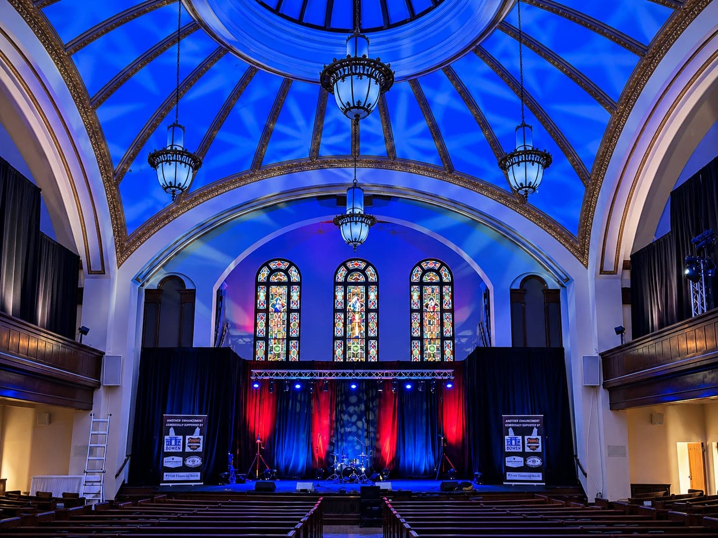 Stage lit in red and blue beneath a domed ceiling washed with blue light