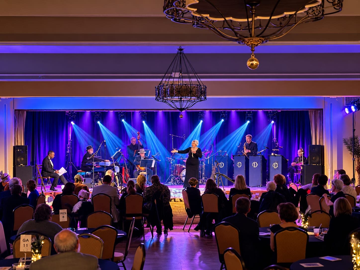 Band and singer on a ballroom stage under blue and purple lighting, audience at dinner tables